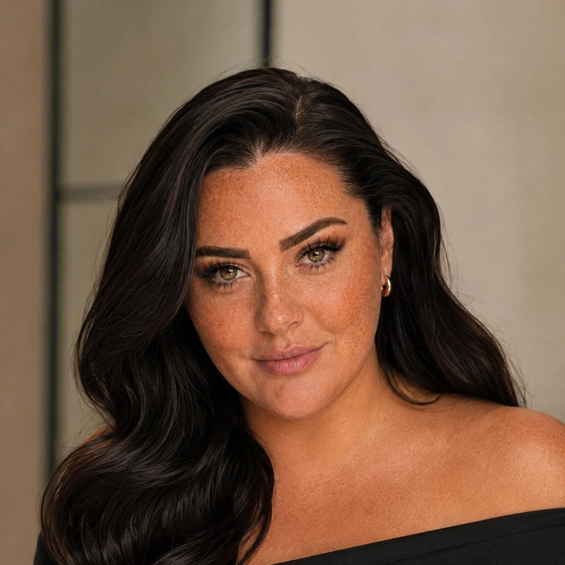 Close portrait of Nina, hair loose over one shoulder, in an off-shoulder black top.