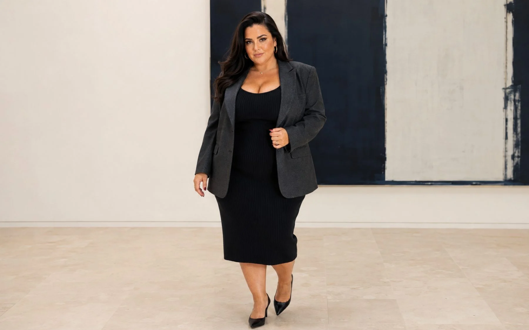 Nina walking through a gallery in a charcoal blazer over a black knit dress.