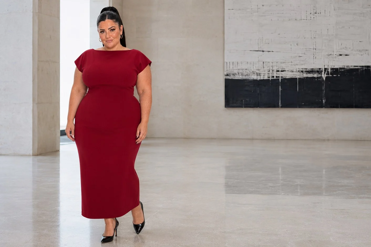 Nina crossing a marble gallery floor in a deep red cap-sleeve maxi dress.