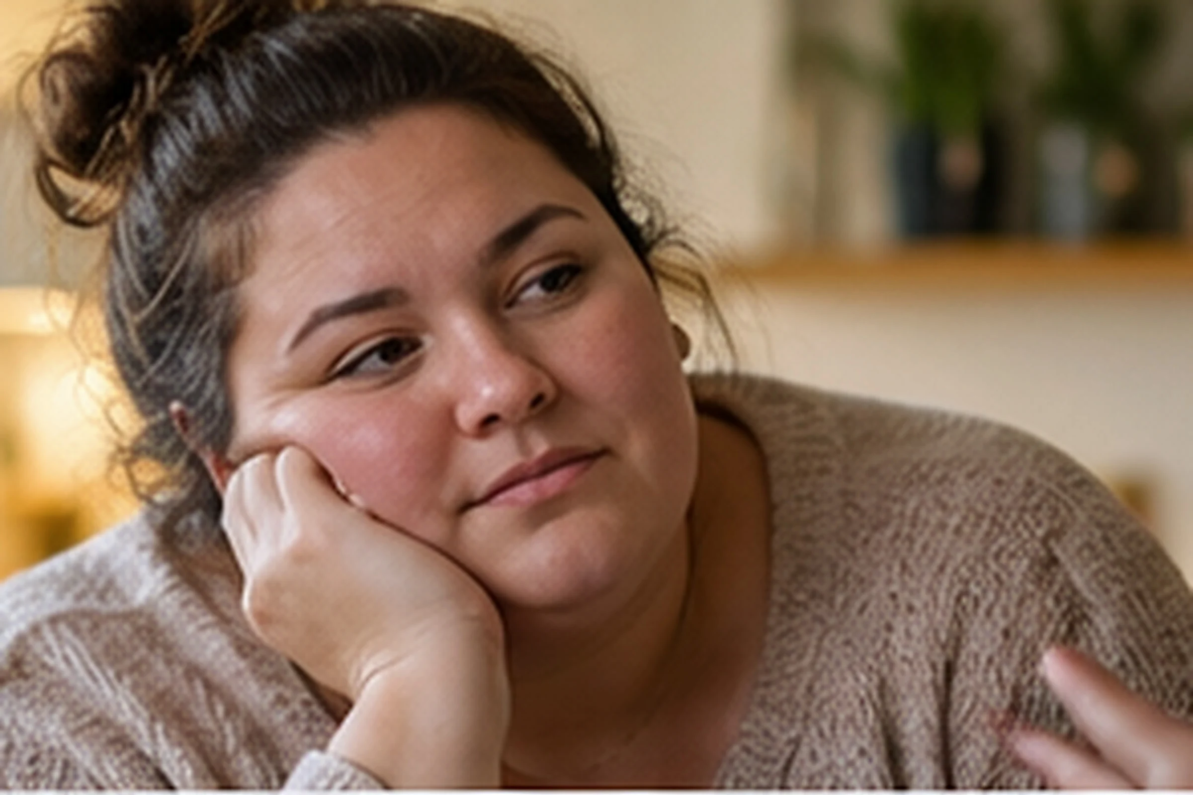 A woman in a knitted jumper rests her cheek on her hand, listening to someone out of frame.