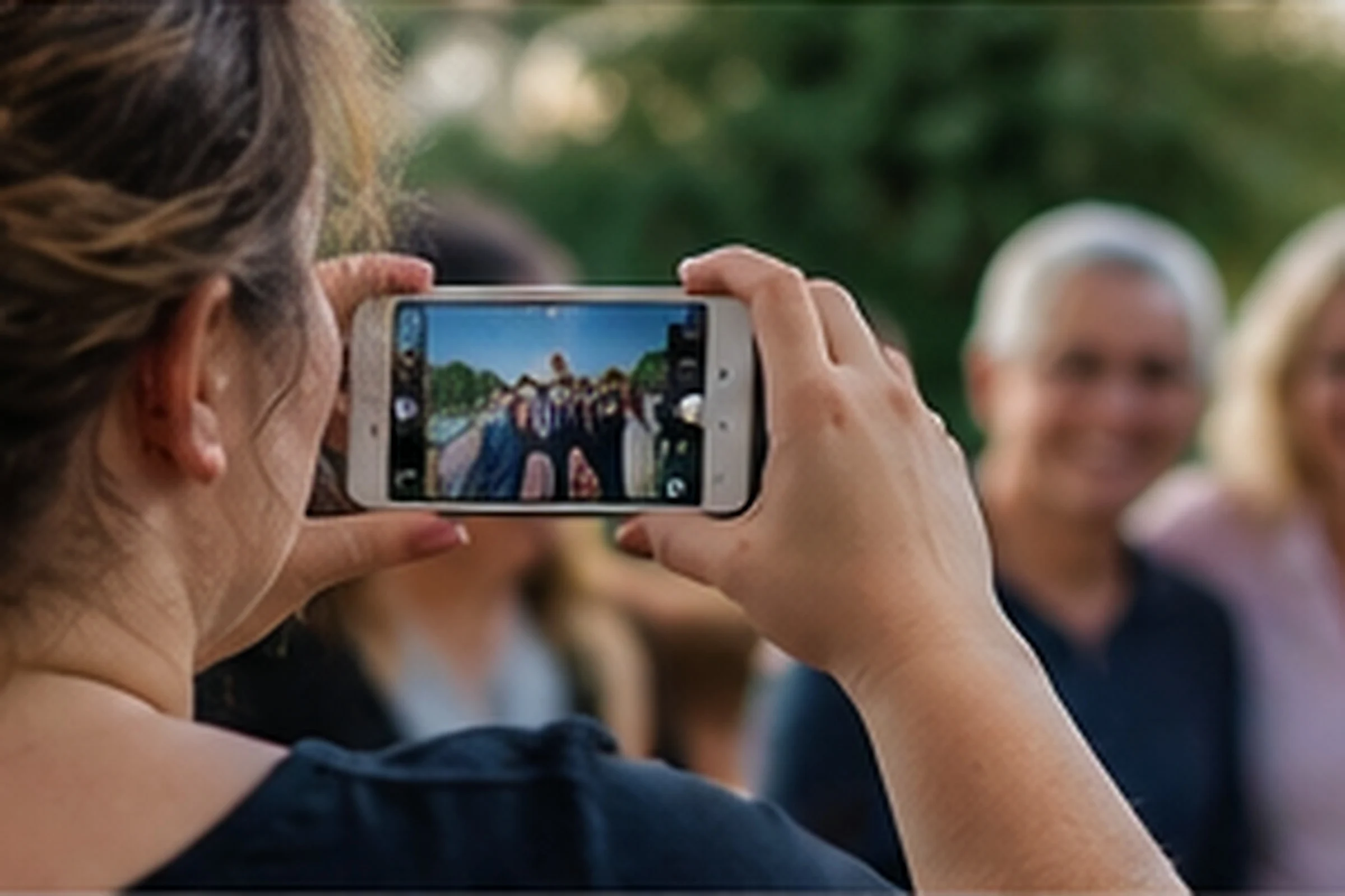 A woman photographs a smiling group of family and friends on her phone.